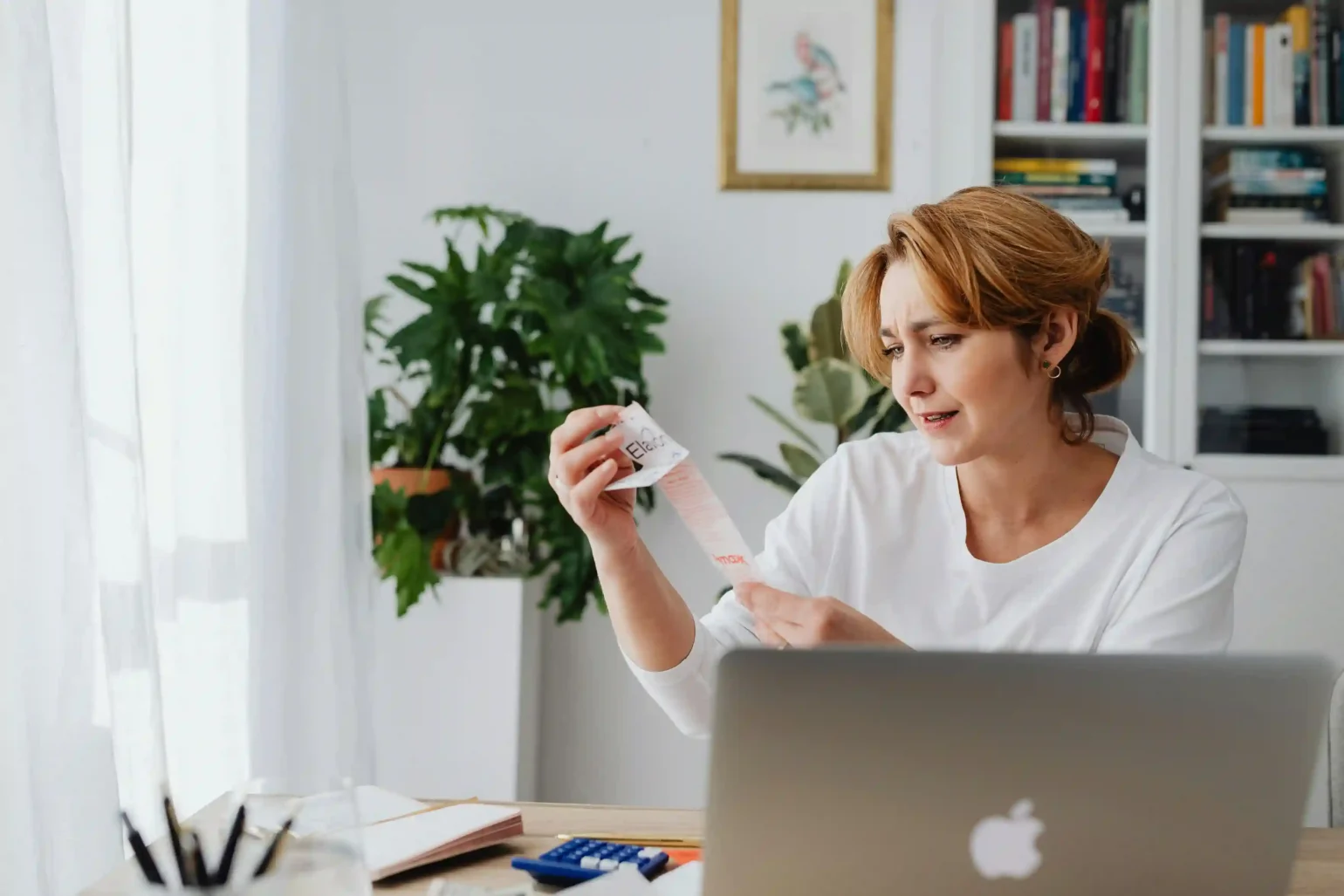 A concerned woman reviewing a long receipt at her desk with a laptop, showing the rising cost of living in the U.S. in 2025.