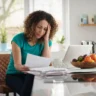 Woman reviewing household bills at a kitchen table, reflecting financial anxiety while managing monthly expenses