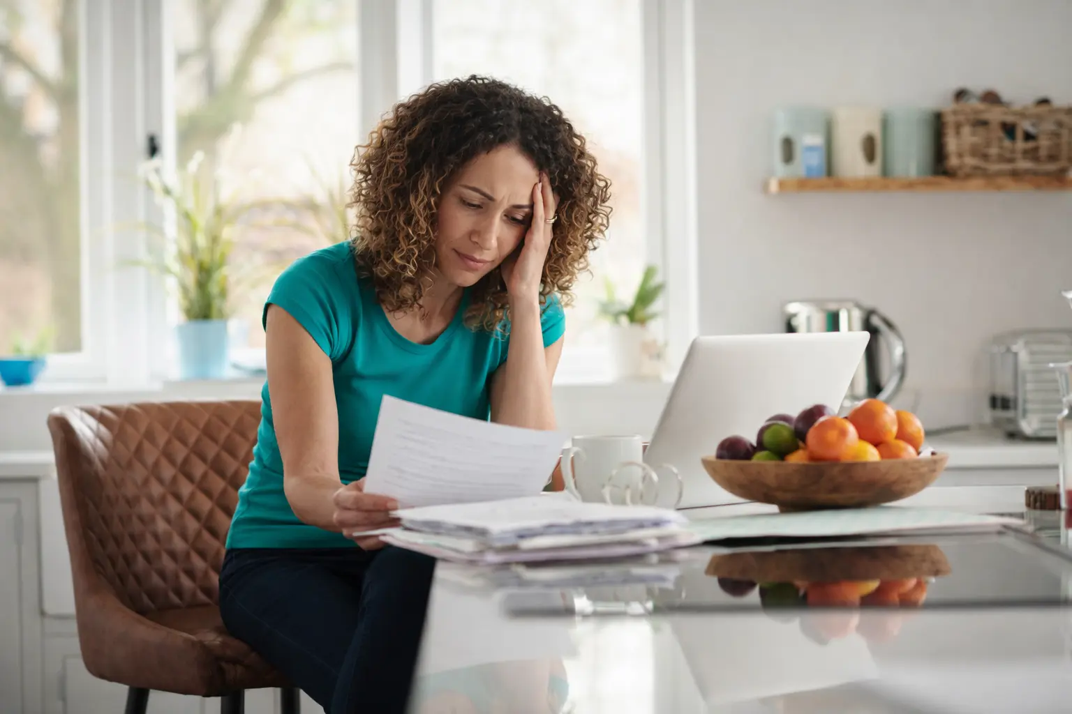 Woman reviewing household bills at a kitchen table, reflecting financial anxiety while managing monthly expenses