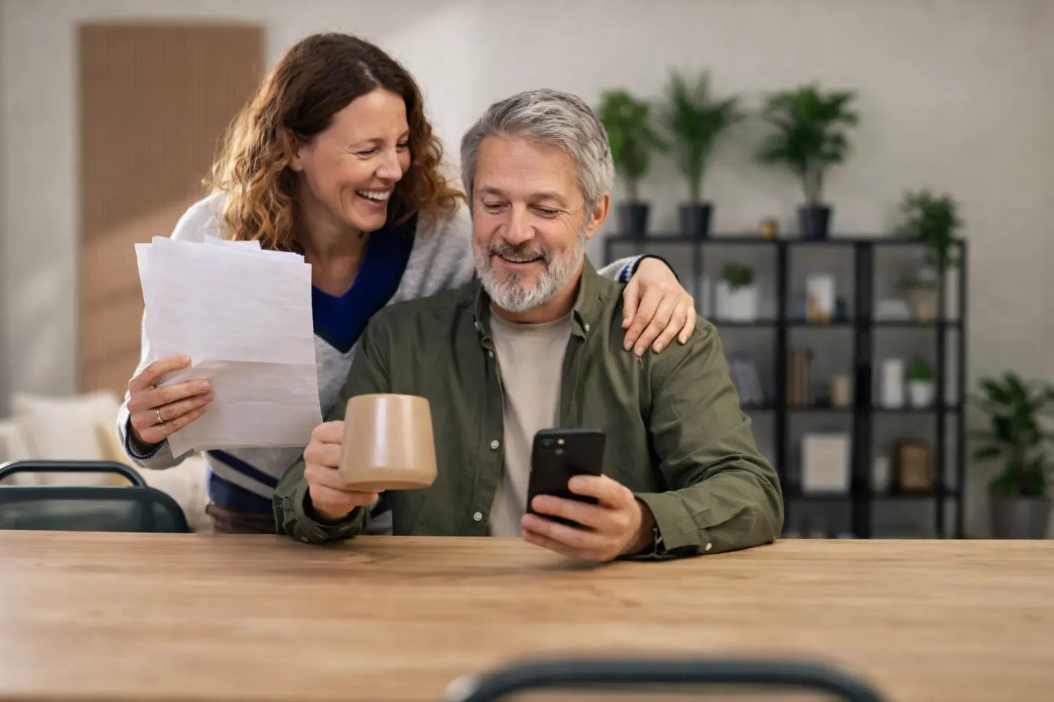 Couple checking a mobile banking app while reviewing financial paperwork as a deposit wave hits bank accounts today across the U.S.