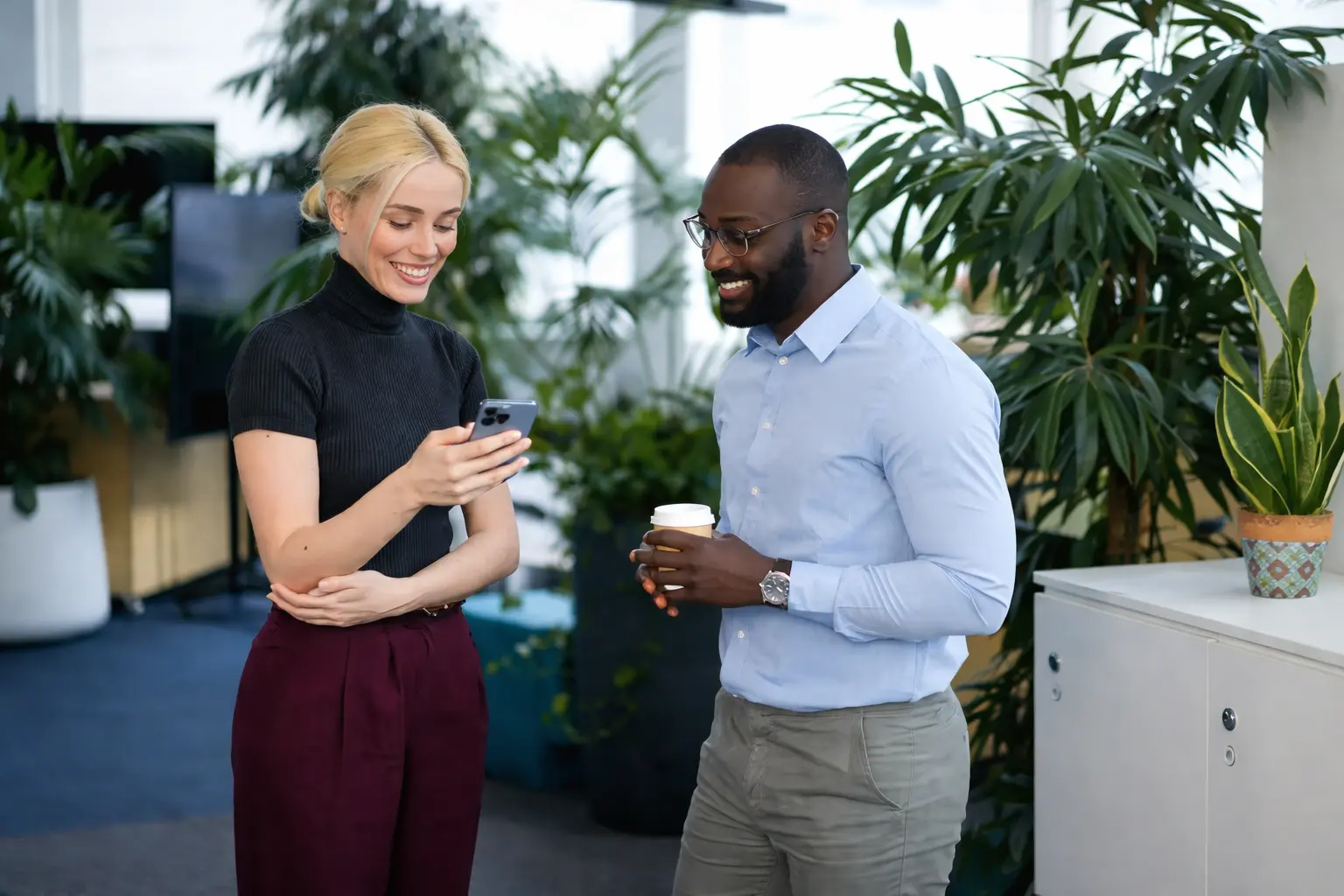 Two coworkers checking a smartphone after one direct deposit arrives earlier than another