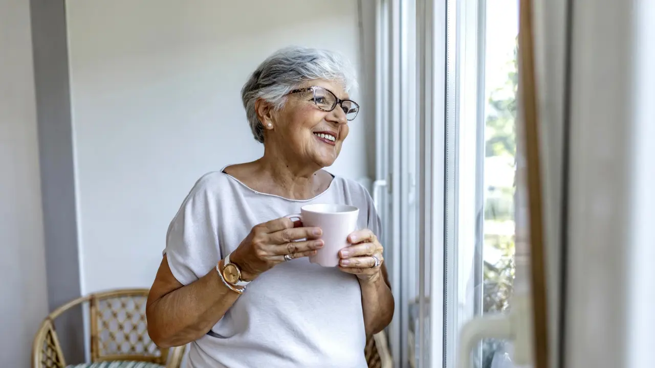 Retired woman looking out a window while considering her Social Security claiming decision
