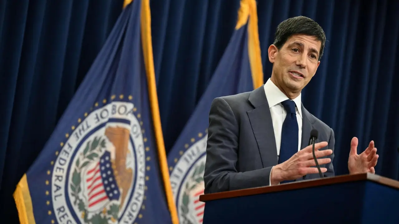 Kevin Warsh speaking at a podium with Federal Reserve flags behind him