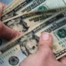 Hands counting U.S. dollar bills as Social Security policymakers debate higher payroll taxes on high earners.