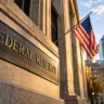 Editorial illustration of a Federal Reserve sign and American flag outside a financial building