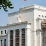 Federal Reserve headquarters building in Washington, D.C., with an American flag and construction scaffolding.