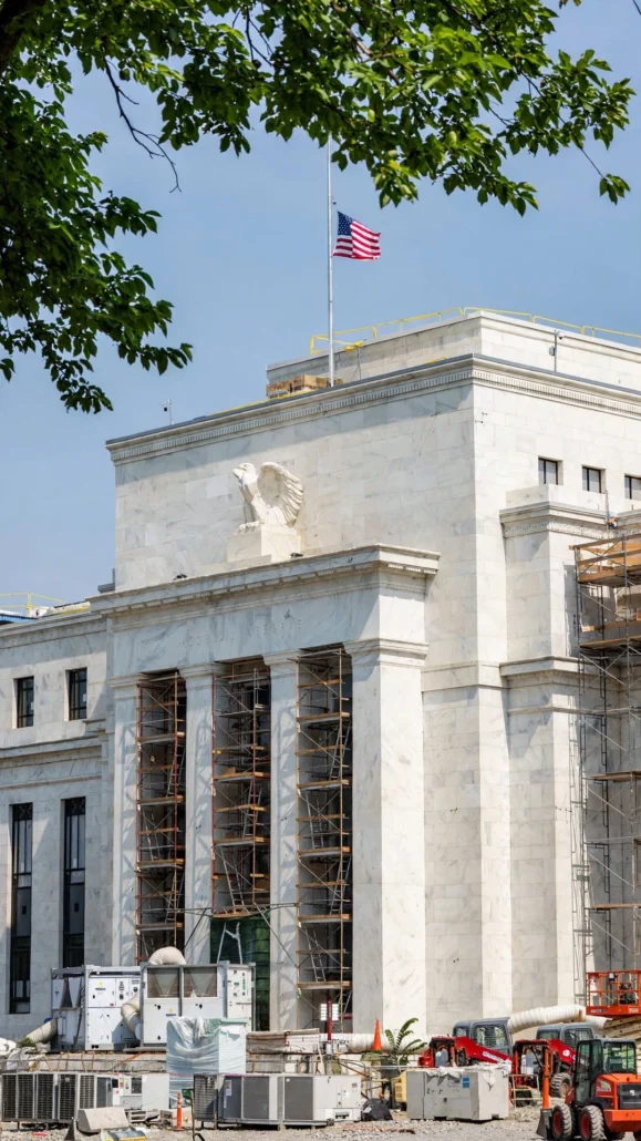 Federal Reserve headquarters building in Washington, D.C., with an American flag and construction scaffolding.