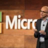 Microsoft CEO Satya Nadella speaking in front of a Microsoft logo at a company event.