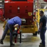 Two manufacturing workers assembling industrial machinery inside a factory as the Philadelphia Fed manufacturing index falls to 20.9 in October 2026.