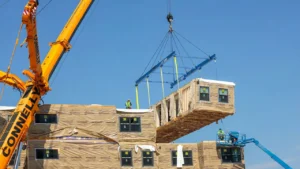 Latest U.S. Financial News and Analysis 16 A crane lifts a prefabricated housing module into position at a residential construction site.