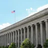 U.S. Treasury Department building in Washington, D.C., with an American flag flying above its columns.
